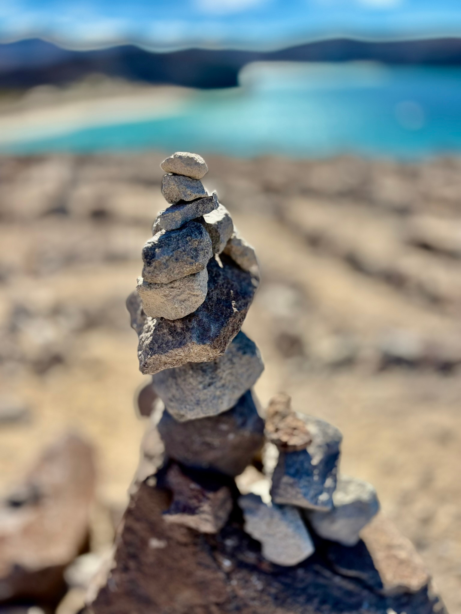 A stacked stone trail marker beside turquoise water